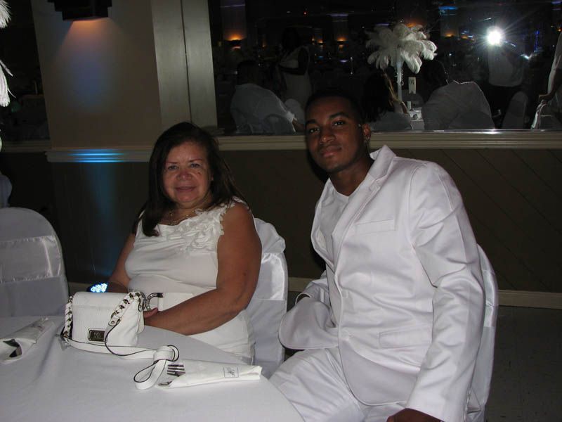 Woman and man at a table, both wearing white. The man is smiling. Formal event setting.