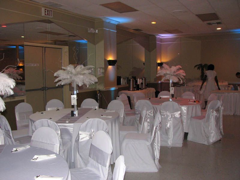 Tables set for a formal event in a banquet hall, decorated with white fabric and feather centerpieces.