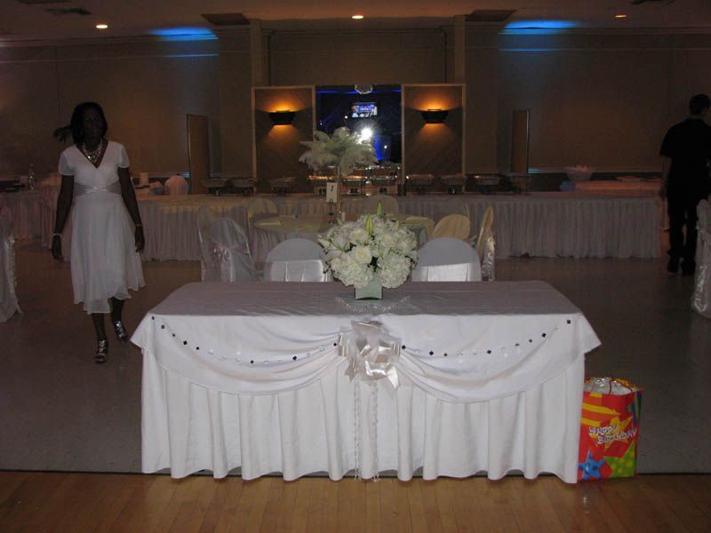 Wedding reception, bride in white dress walking towards decorated sweetheart table, buffet in background.