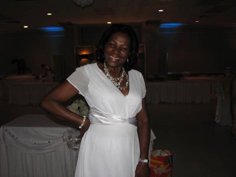 Woman in white dress smiling, hand on hip, in a banquet hall.