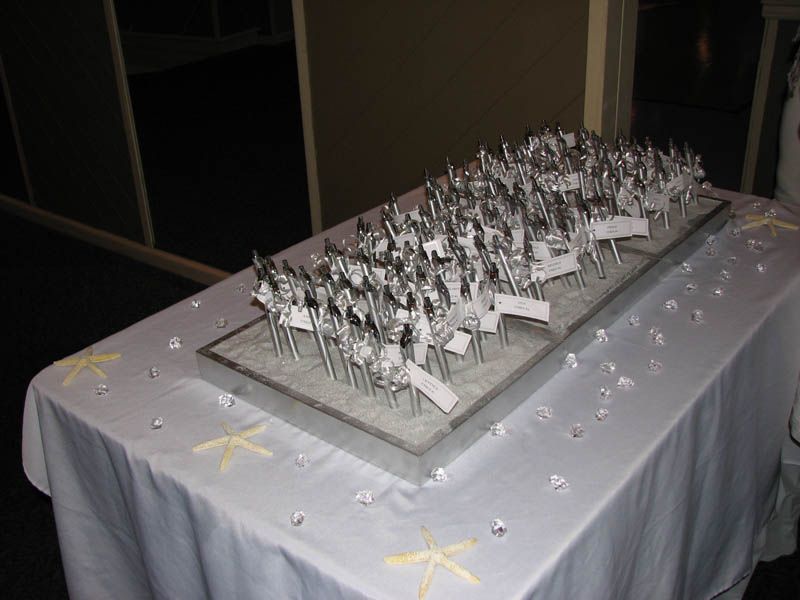 Table with silverware, each with a name tag, arranged on a gray platform, decorated with starfish and crystals.