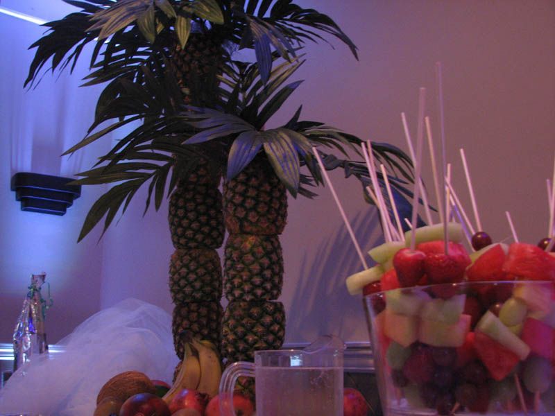 Tropical fruit display with pineapple palm trees and skewers of fruit.