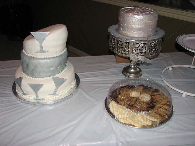 Cakes on a table. One multi-tiered cake with martini glass design, one small silver cake, and a cookie platter.