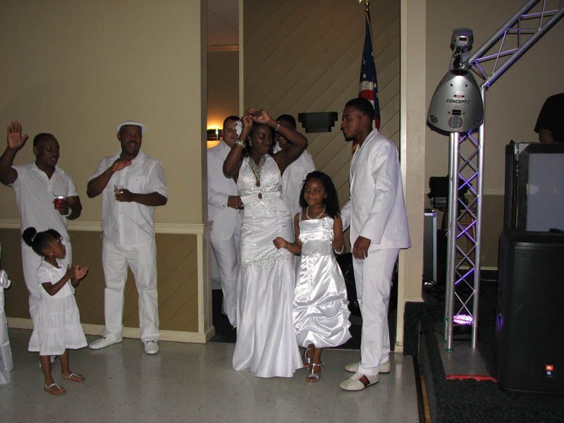People in white formal wear dancing at an event, with stage lighting.