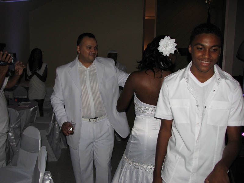 People in white attire at an event, including a bride with a flower in her hair, and two men, one in a white suit.