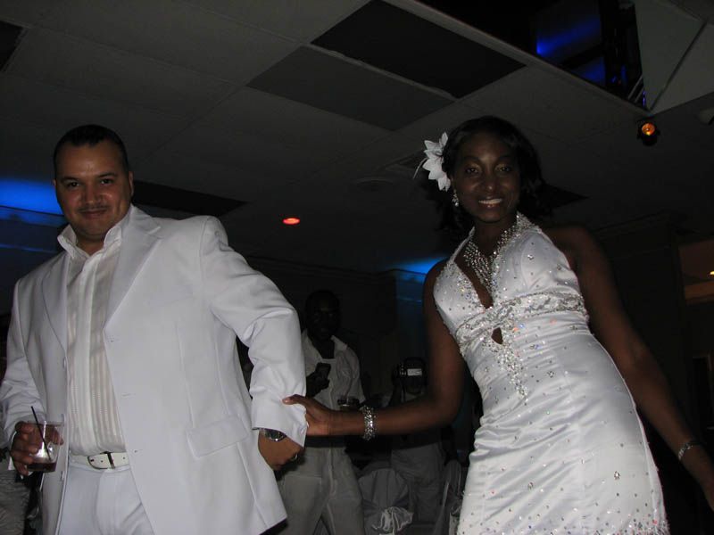 Couple dancing at an event, man in white suit, woman in white dress.