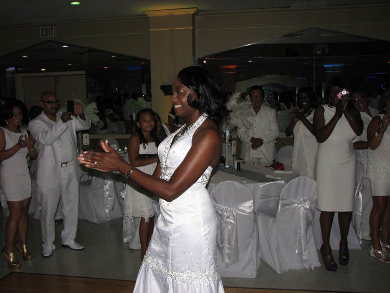 Woman in white dress clapping at a party, surrounded by people in white clothing.