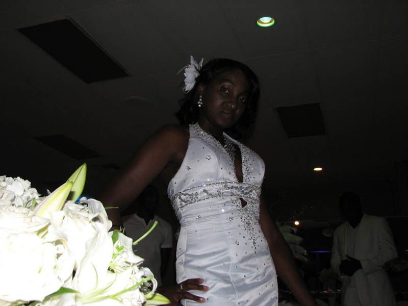 Woman in white dress with floral bouquet; event setting.
