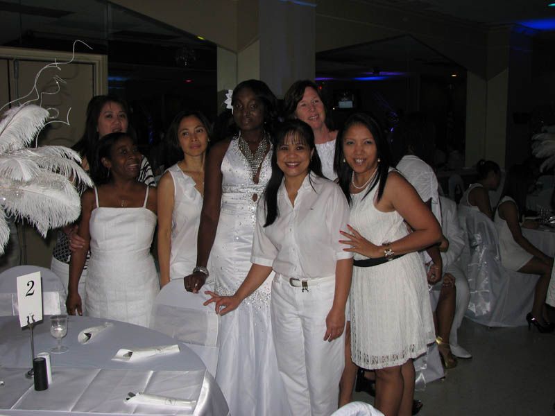 Group of people in white clothing pose at a party, likely a dinner.