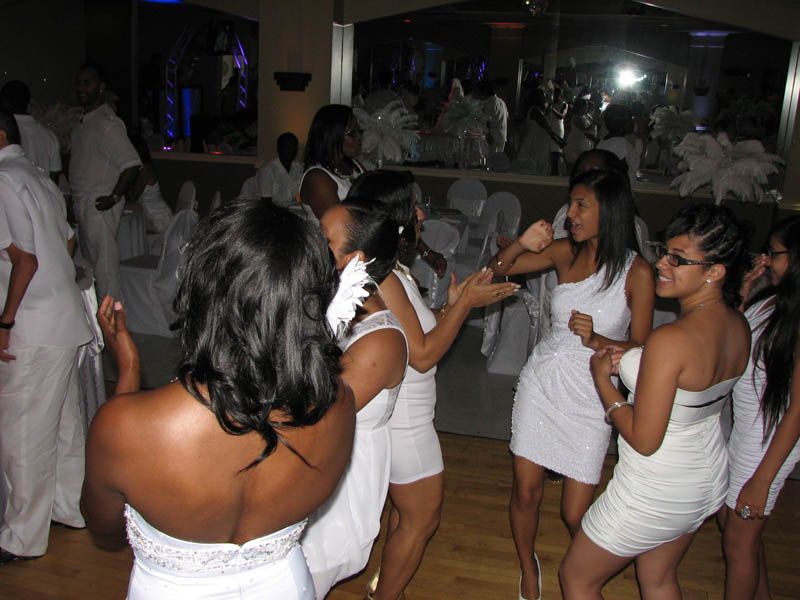 People dancing in a well-lit room; most are wearing white.