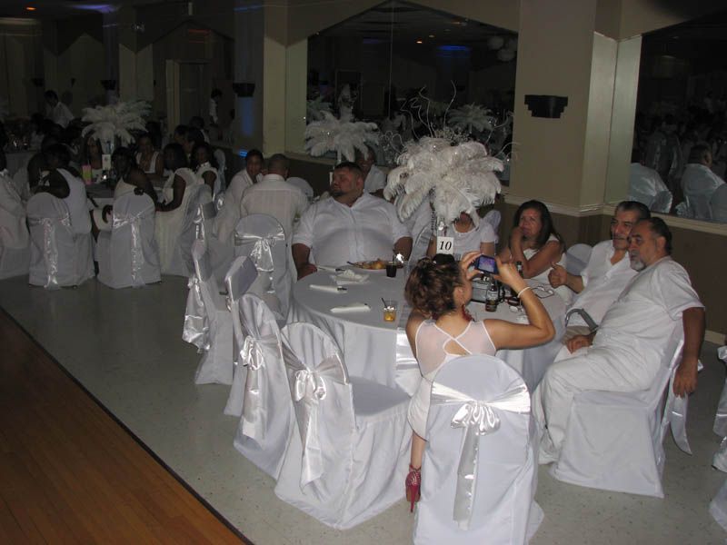People at a formal event, seated at tables with white decor. Woman takes a photo.