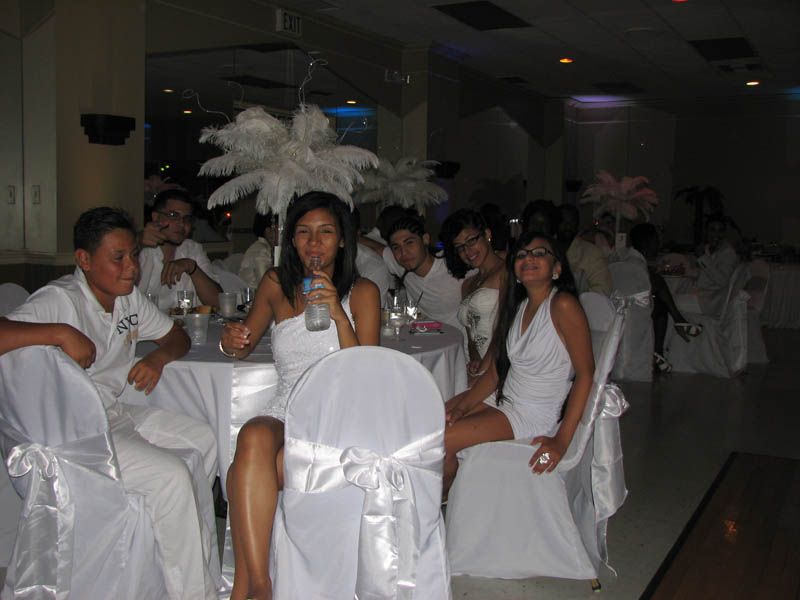 People in white outfits at a party, seated at a table. Feather decorations and white tablecloths.