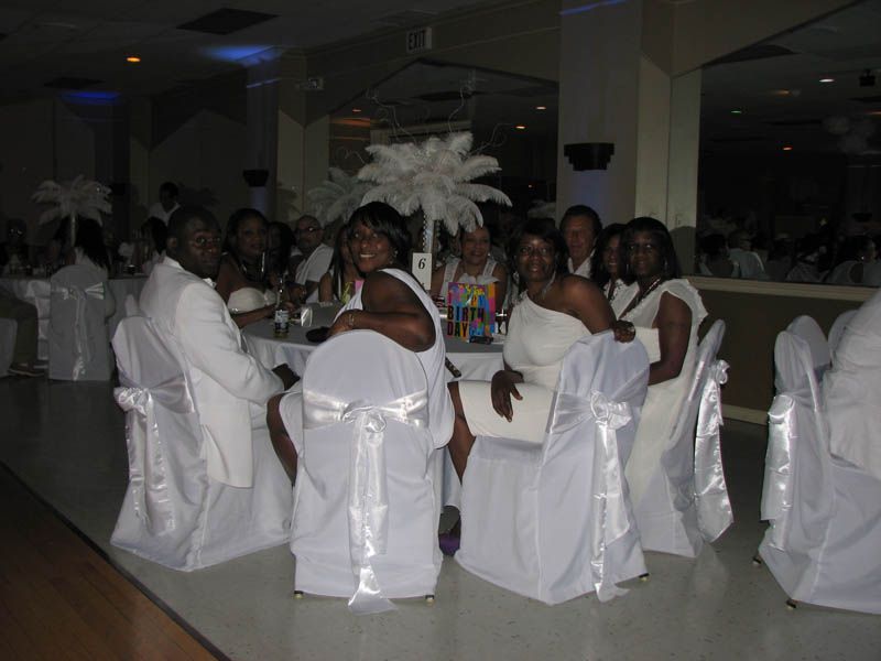 Group of people in white attire seated at a table, smiling at a formal event.