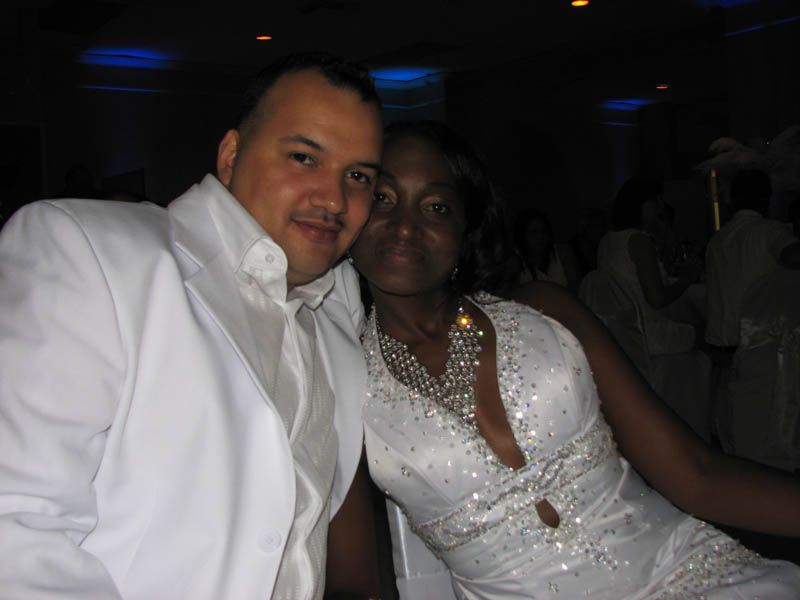 Man in white suit and woman in white dress, smiling, indoors.