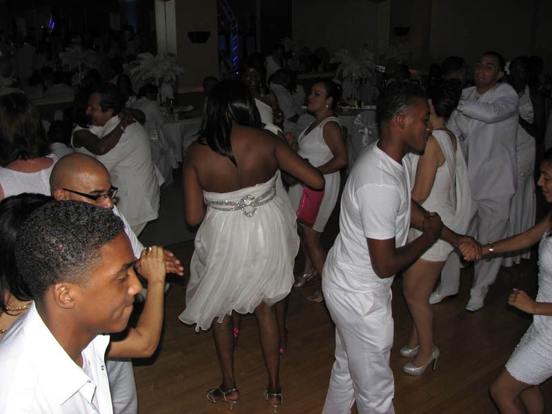 People dancing in a crowded hall, mostly wearing white.