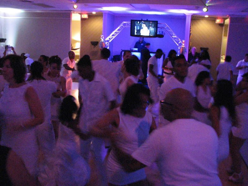 People dancing in a brightly lit room, all wearing white clothing.