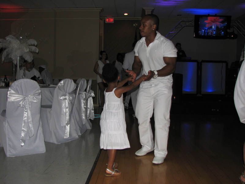 Man dances with a young child at an event. Both are wearing white.