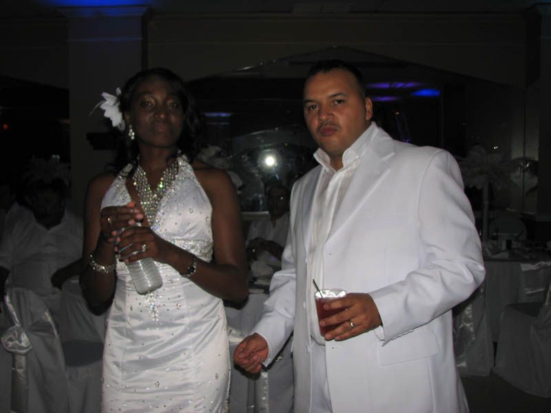 Woman in white dress and man in white suit holding drinks in a well-lit room.