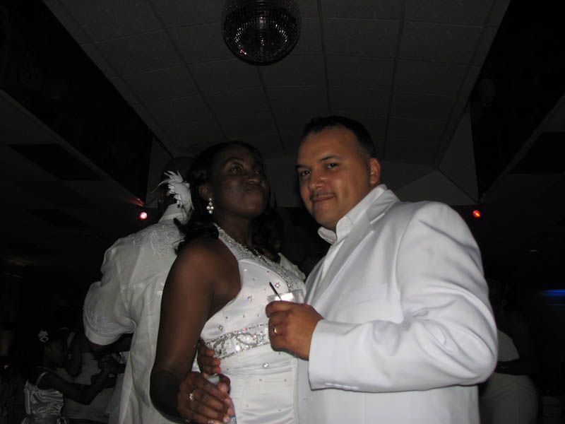 Couple in white attire, possibly at a wedding reception, inside with a disco ball and others in the background.