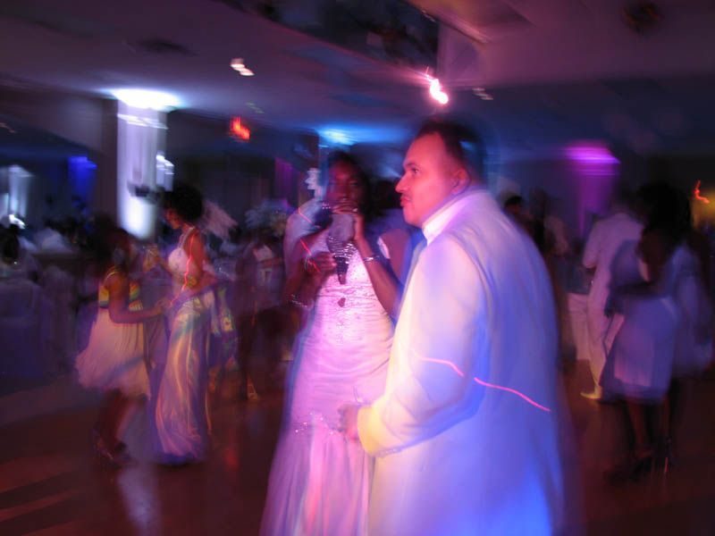 People dancing at a wedding reception under colorful lights.