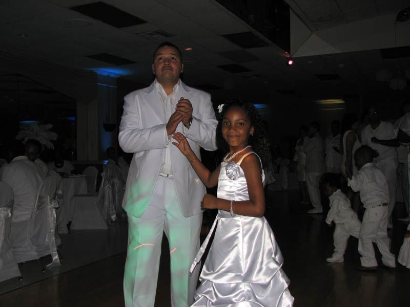 Man and girl in white formal attire dancing in a ballroom.