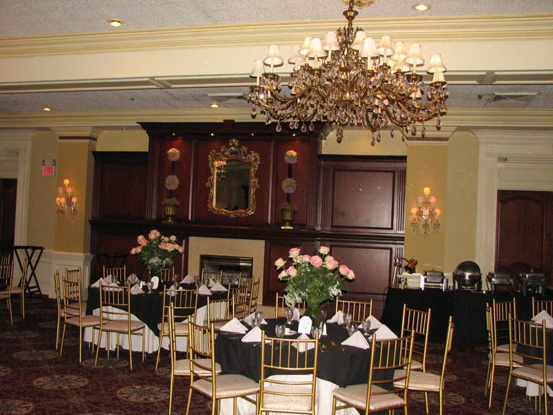 Formal dining room with tables set for a party, large chandelier, fireplace, and buffet.