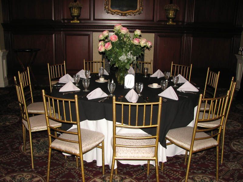 Round table set for a formal event with black tablecloth, gold chairs, and floral centerpiece.