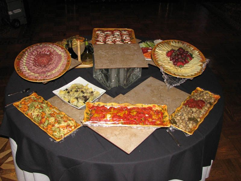 Buffet table with various foods: meats, cheeses, tarts, and a vegetable display on a black tablecloth.