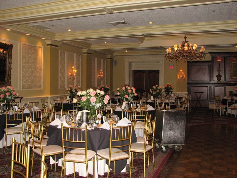 Banquet hall with round tables set for a formal event. Tables have black tablecloths, gold chairs, and floral centerpieces.