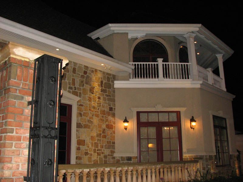 Night view of a two-story building with brick, stone, and stucco exterior. Balcony and red doors are visible.