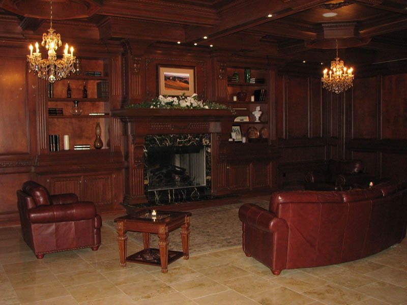 Formal library lounge with wood paneling, fireplace, leather furniture, and chandeliers.