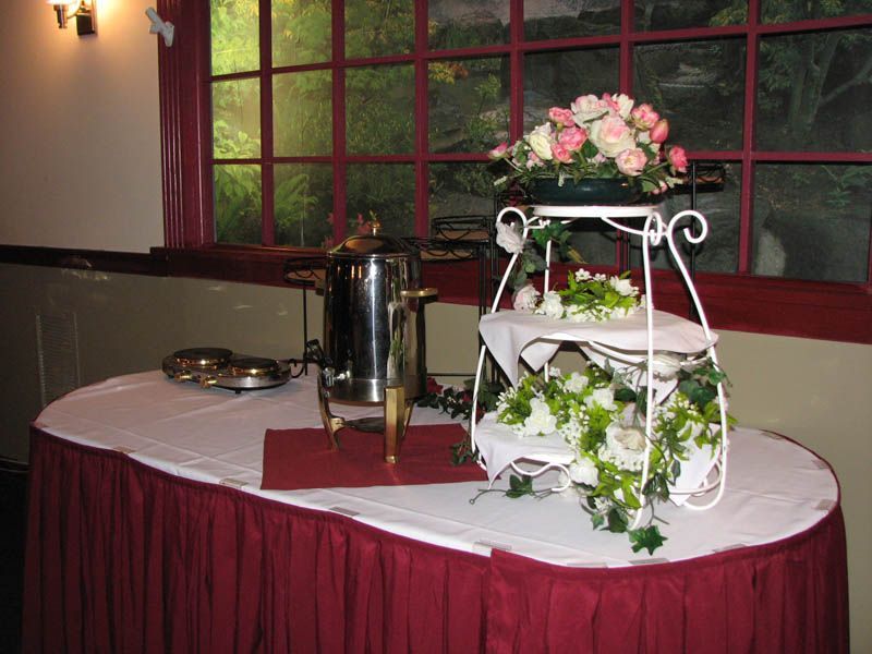 Coffee station with a tiered server holding flowers and pastries. Red and white tablecloth.