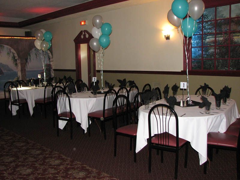 Dining room with round tables, white tablecloths, black chairs, balloons.