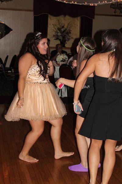 Three young people dancing barefoot at a formal event; the woman in a peach dress is facing the camera and smiling.