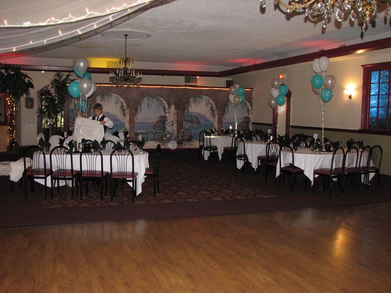 Banquet hall with tables, balloons, and decorative murals; hardwood floors and dark carpet.