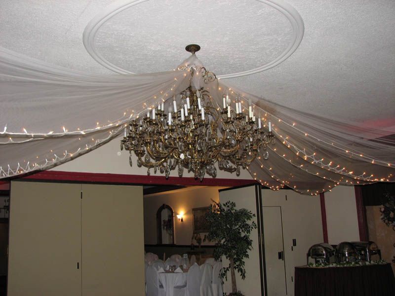 Chandelier with hanging lights and fabric decorations in a room, with folding doors and buffet tables.