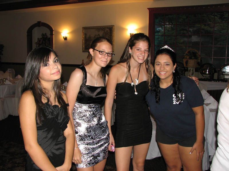 Four young people smiling in a formal setting, dressed in dresses and a t-shirt.