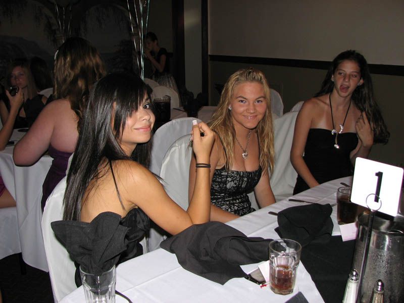 Three women at a table, one holding a cigarette, in a restaurant. White tablecloth, black dresses, table number one.