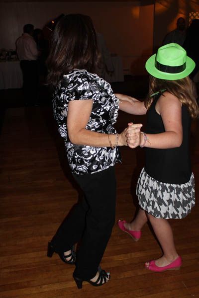 Woman and girl dancing at a party; the girl wears a green hat and black and white skirt.