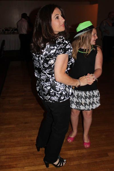 Two women dancing at a party; one in black and white patterned top, other in a black dress and hat.