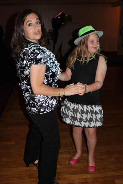 Woman and child dancing, wearing black and white patterned outfits, a neon green hat, and pink shoes.