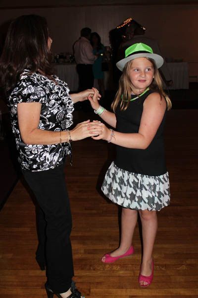 Woman and child dancing at an event; the child wears a hat and skirt, the woman a patterned shirt and pants.