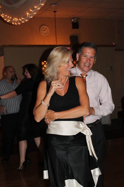 Couple dancing in a dimly lit ballroom; woman in black dress, man in a pink shirt.