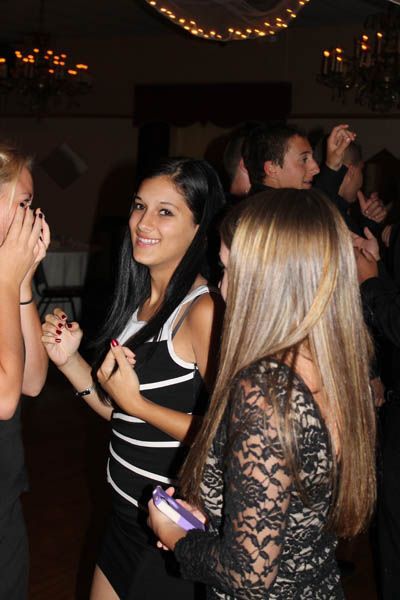 Three young adults dancing at a party; woman in black-white striped top smiles.