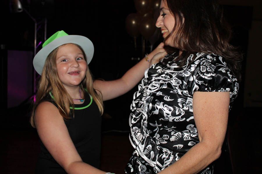 Girl in glowing hat dances with woman in a black and white floral top, indoors.