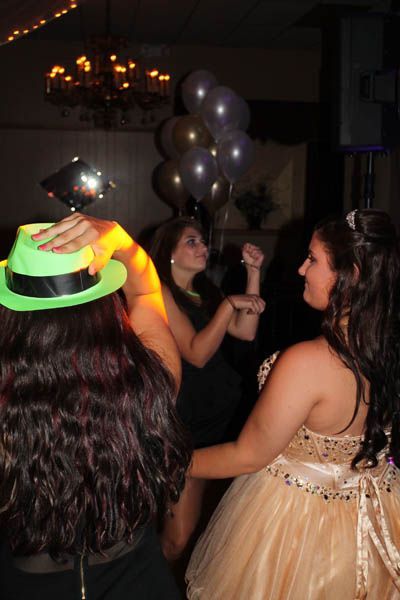Three people dancing in a party setting. Balloons in the background. One person wears a bright green hat.