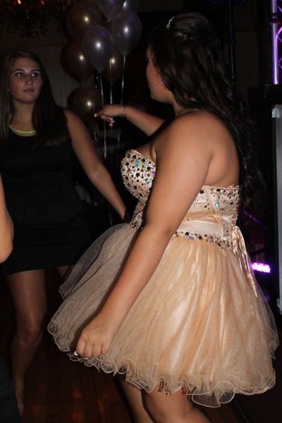 Woman in a formal dress dancing at a party, other person watching. Balloons in background.