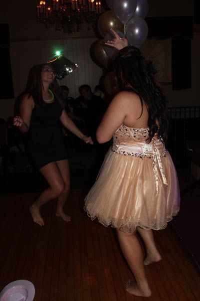 Two people dancing barefoot at a party with balloons. One wears a short, beige dress, the other a black dress.