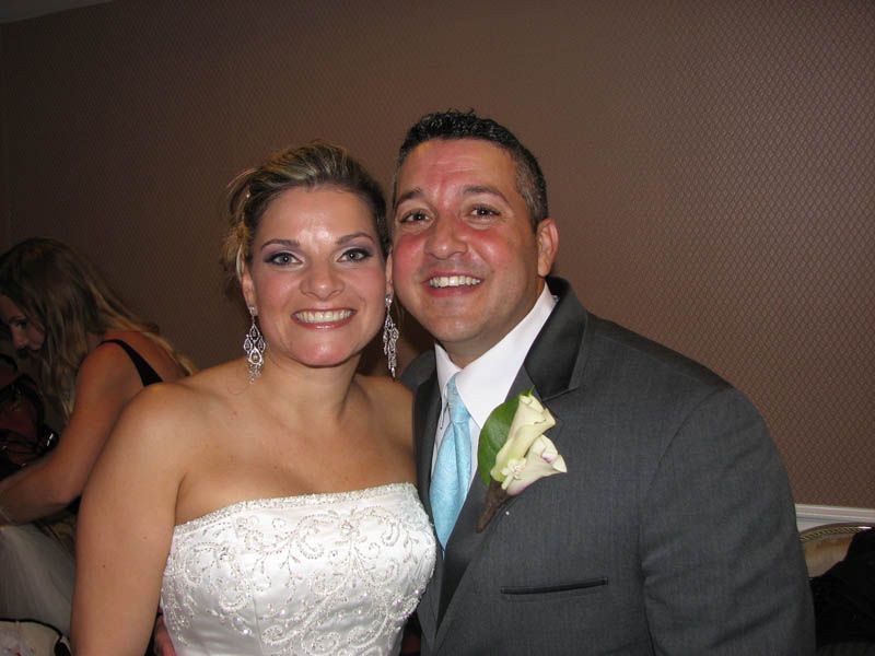 Bride and groom smiling; bride in white strapless dress, groom in gray suit with turquoise tie and boutonniere, interior.