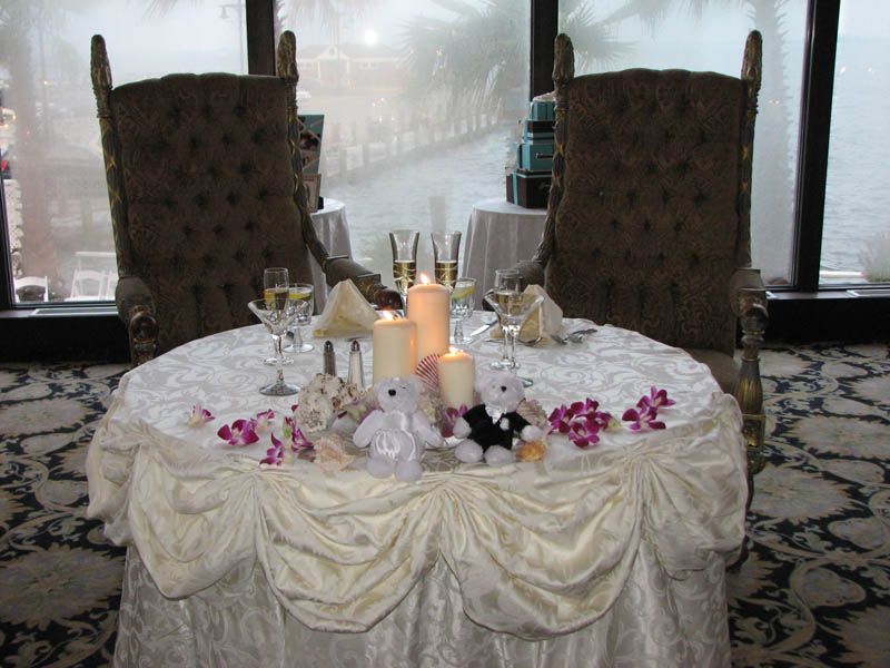 Wedding table setting with ornate chairs, candles, champagne flutes, flowers, and stuffed animals.